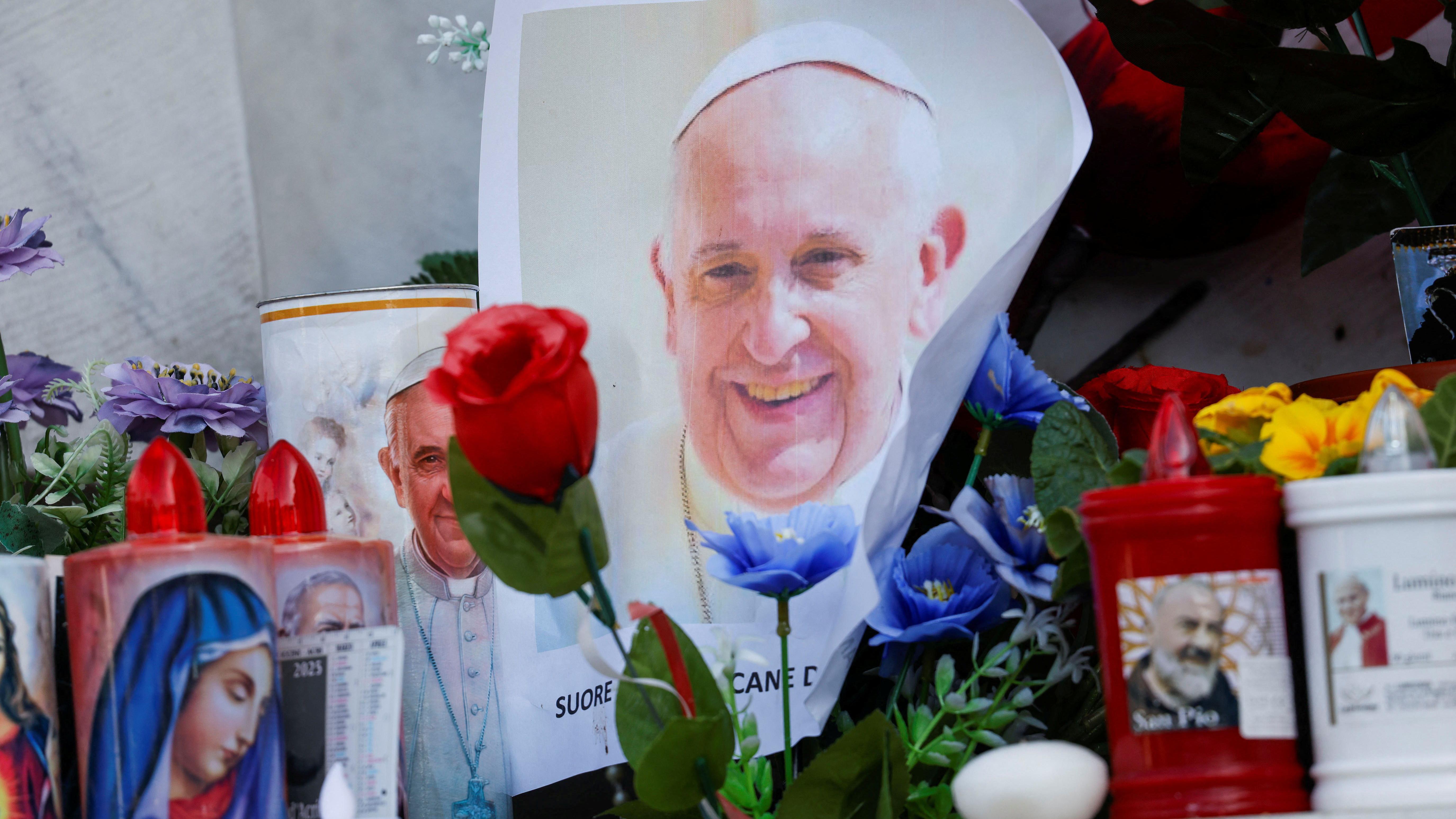 Uma foto do Papa Francisco ao lado de velas e flores na base da estátua do falecido Papa João Paulo II, do lado de fora do Hospital Gemelli, onde Francisco está internado para tratamento
