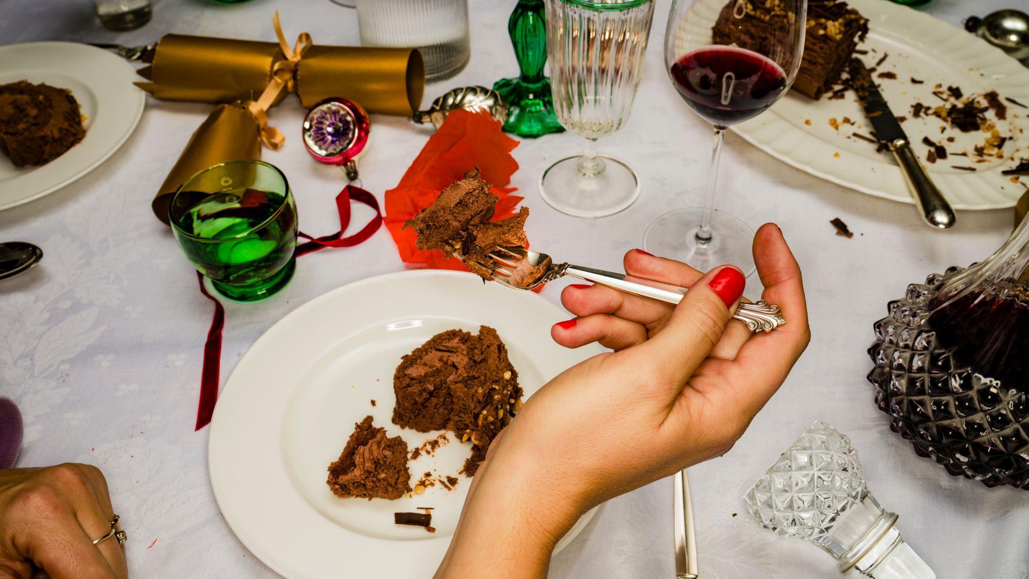 Mão feminina comendo bolo de chocolate ao lado de uma taça de vinho já quase vazia