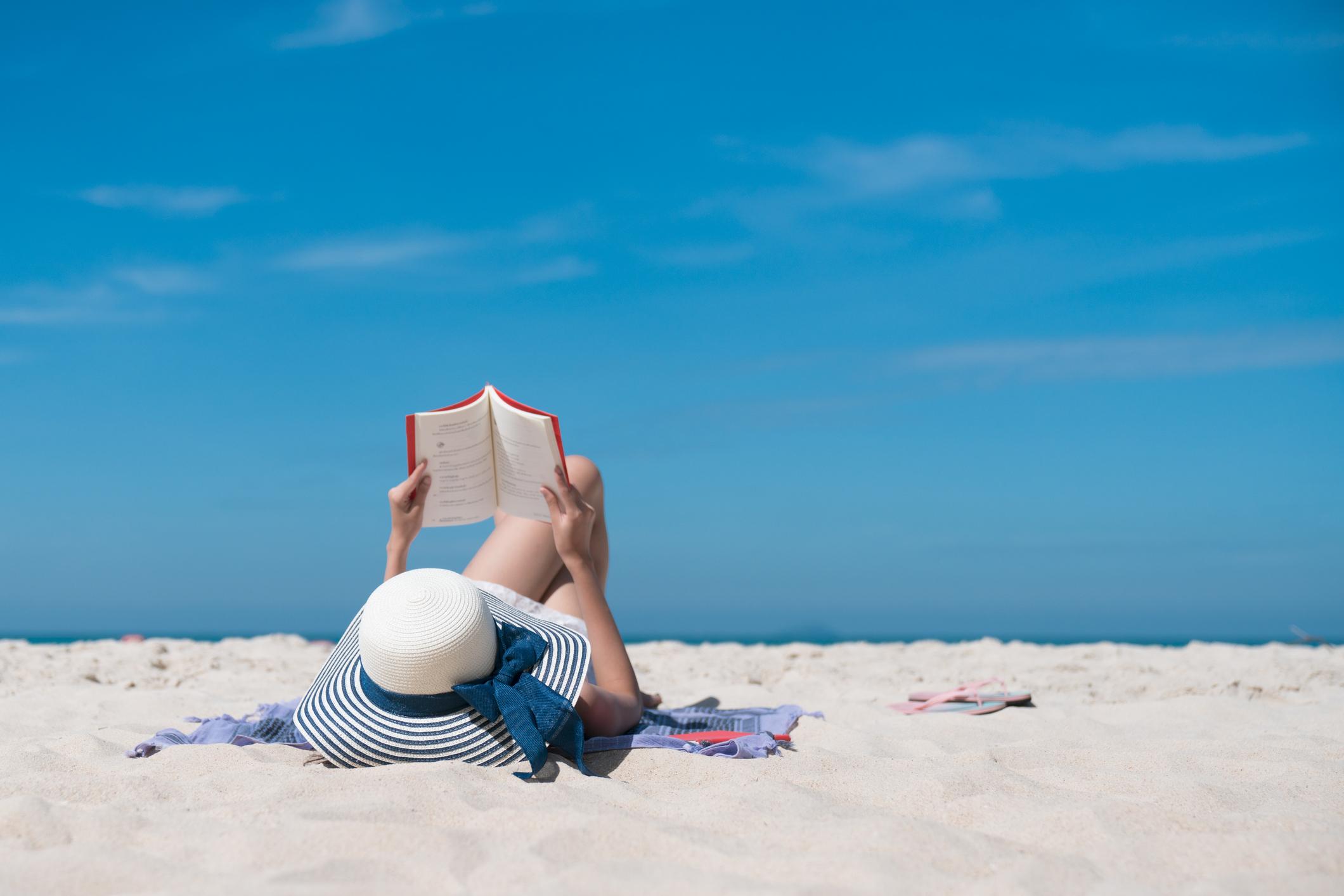 Mulher deitada na praia sozinha lendo um livro