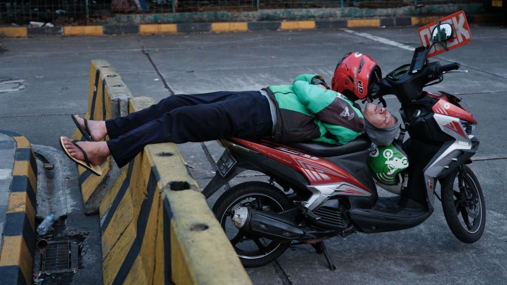 Seorang pengemudi ojek online di Jakarta terlelap di atas sepeda motor.