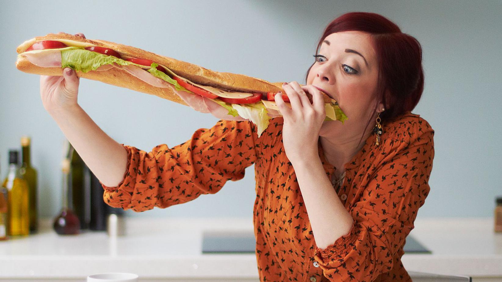 Mujer come un bocadillo gigante.