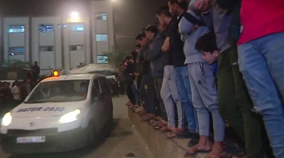خان یونس میں مردوں کی ایک قطار زخمی اٹھائے گاڑی کے سامنے کھڑے ہیں