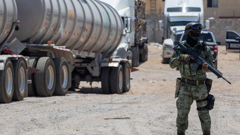 Soldado armado ao lado de caminhão de gasolina.