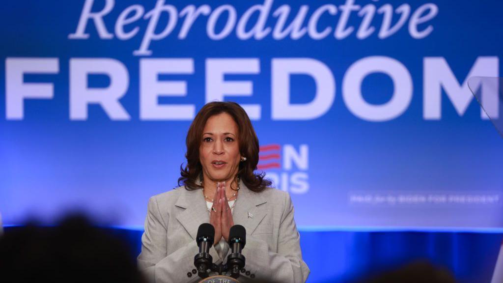 Kamala Harris com uma placa atrás dela que diz 'Liberdade Reprodutiva'