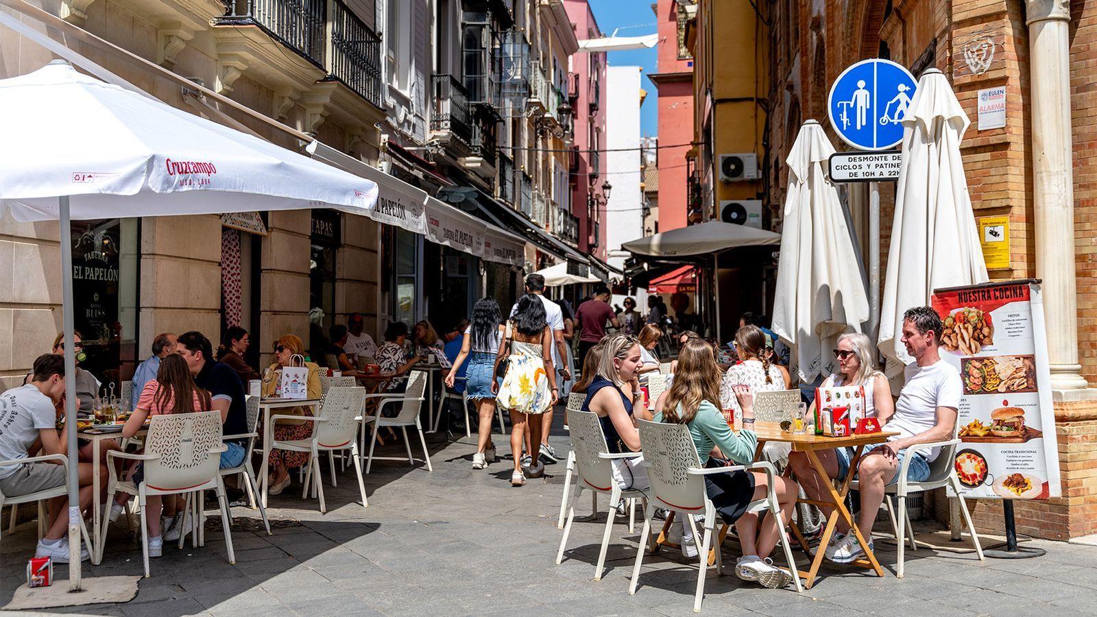 várias pessoas sentadas em cafés distribuídos em rua estreita