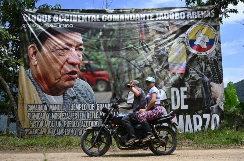 Pessoas andando de moto em frente a cartaz