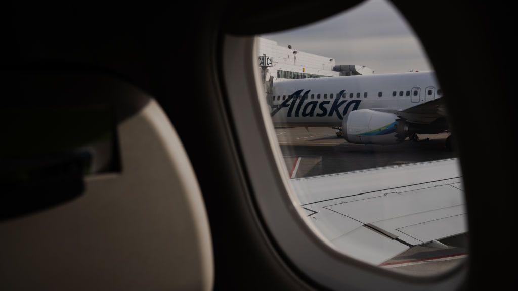 Imagem mostrando um avião da Alaska Airlines pela janela de outro avião.