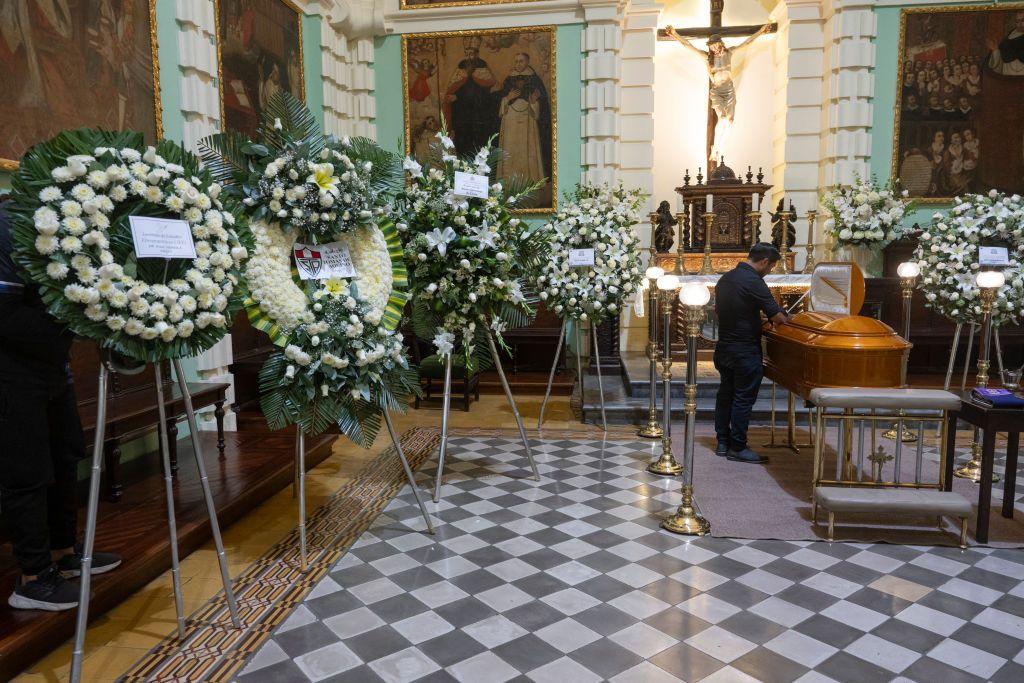 A man pays tribute to the late Peruvian priest and intellectual Gustavo Gutiérrez in a church. The coffin is surrounded by wreaths of white flowers.