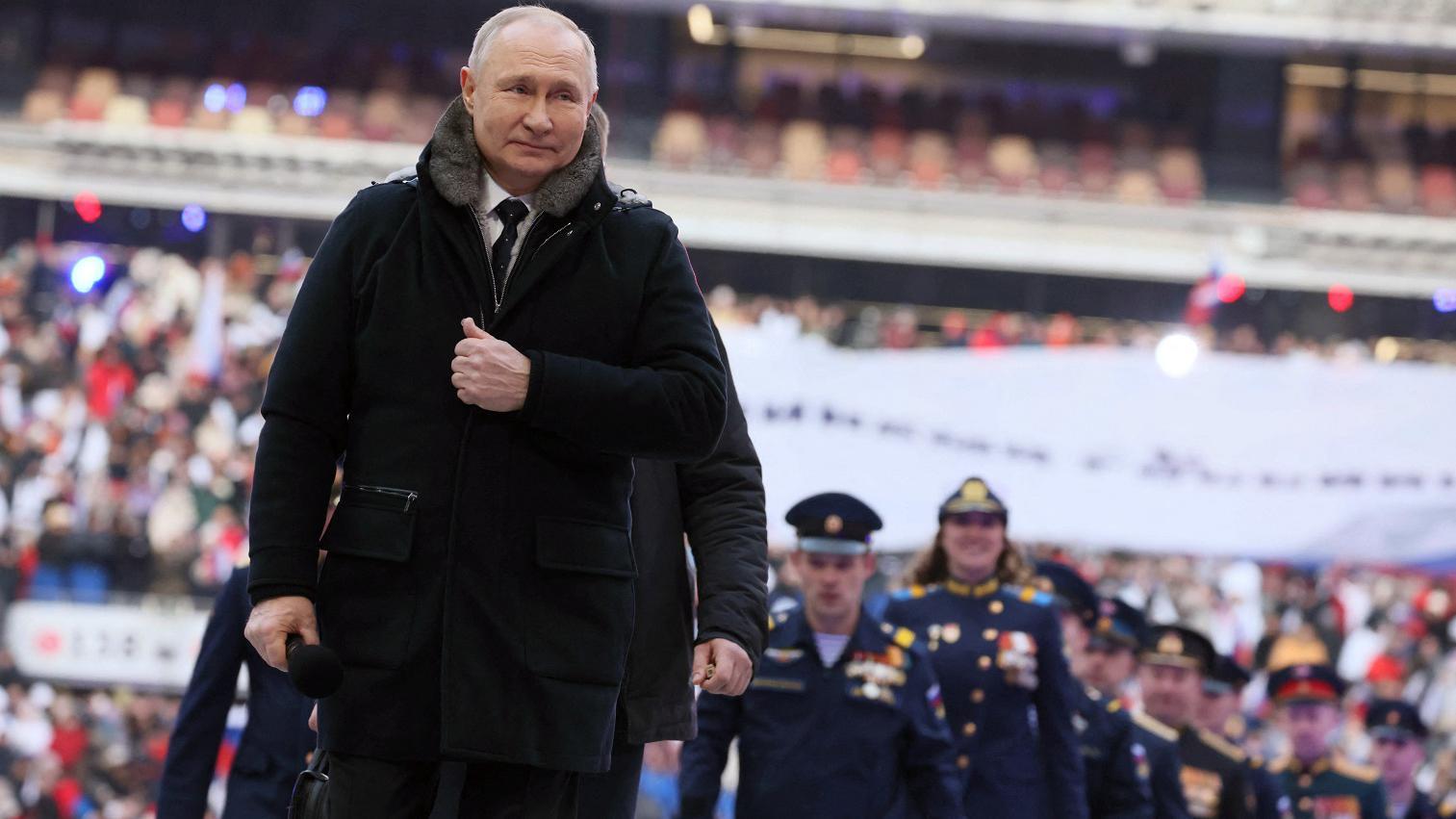 Putin sorrindo em frente a fileira de soldados em evento