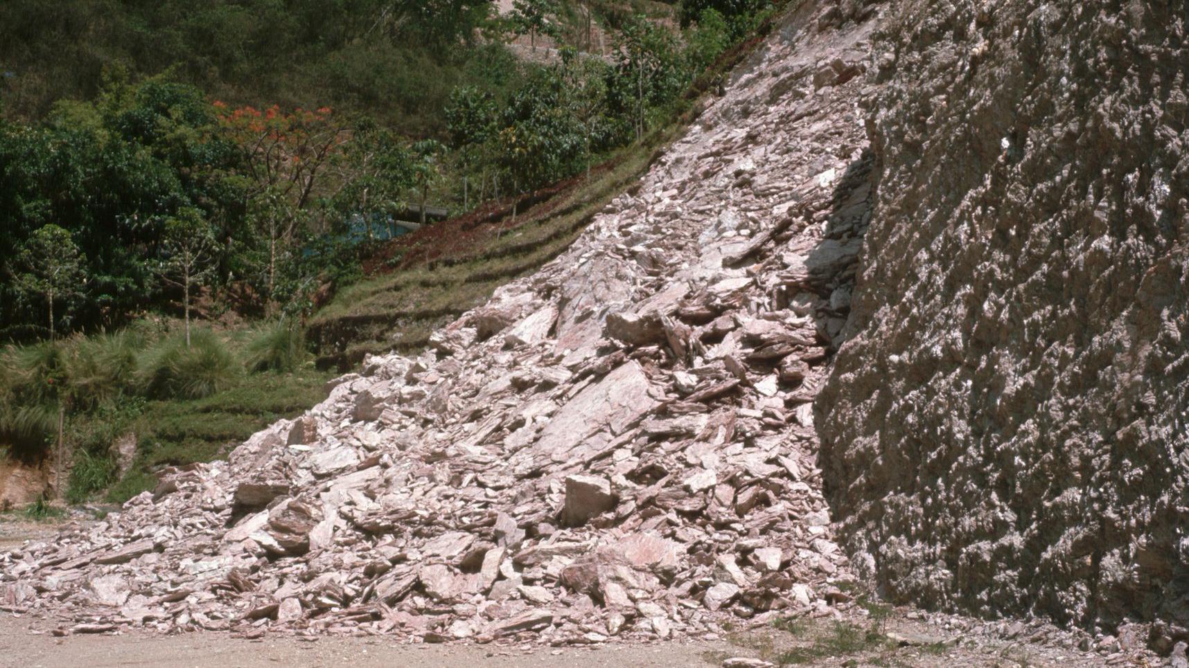 Pile of rocks and debris from a landslide next to a steep, rocky hillside.