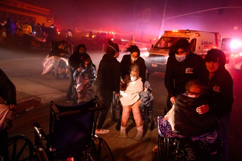 Pacientes idosos são levados em cadeiras de rodas para veículos de emergência enquanto brasas e chamas se aproximam durante o incêndio em Pasadena, na Califórnia