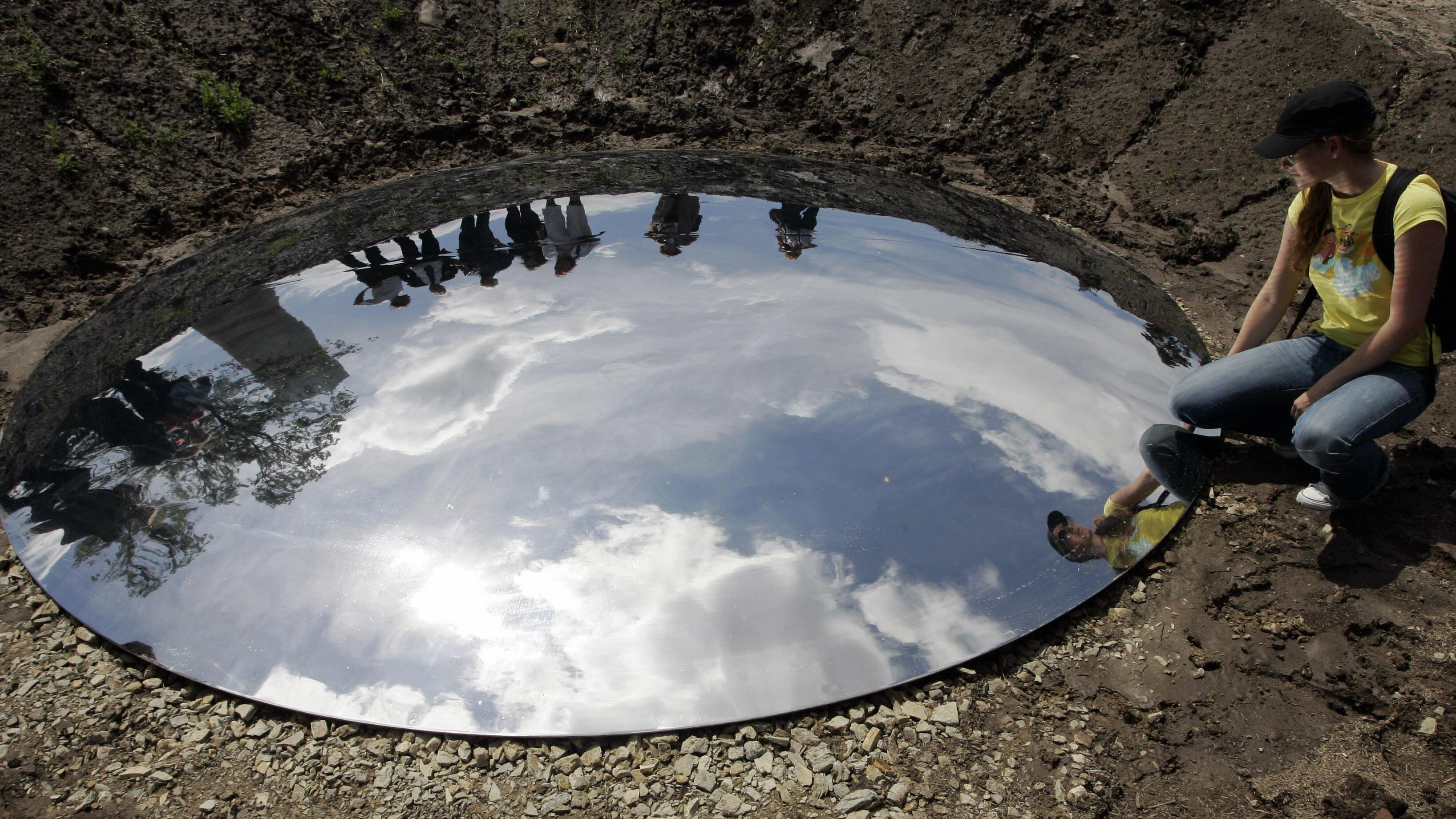 Espelho circular no chão com céu refletido 