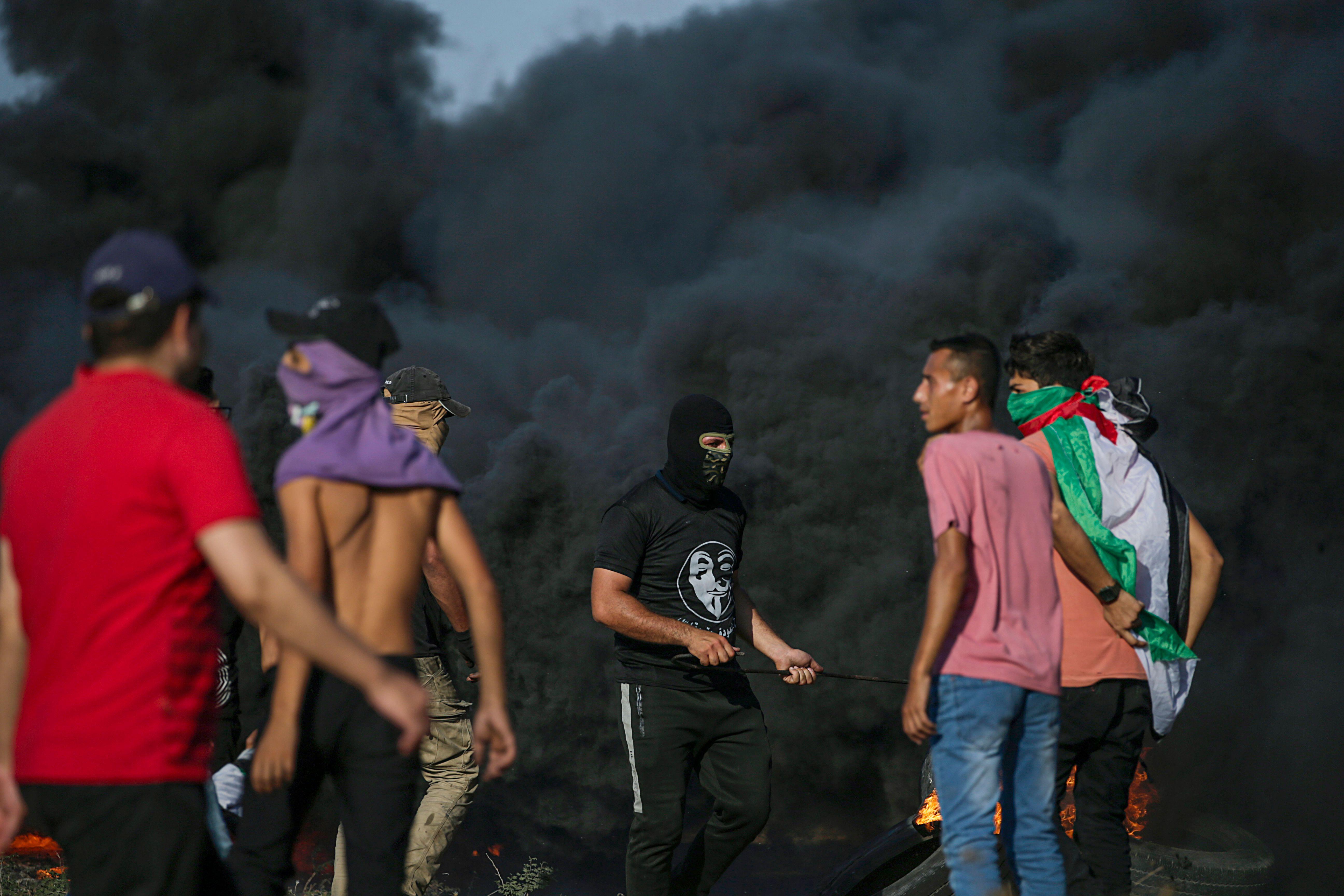 متظاهرون فلسطينيون يقفون بالقرب من الدخان الأسود المتصاعد من الإطارات المحترقة خلال الاشتباكات على الحدود الشرقية لقطاع غزة.
