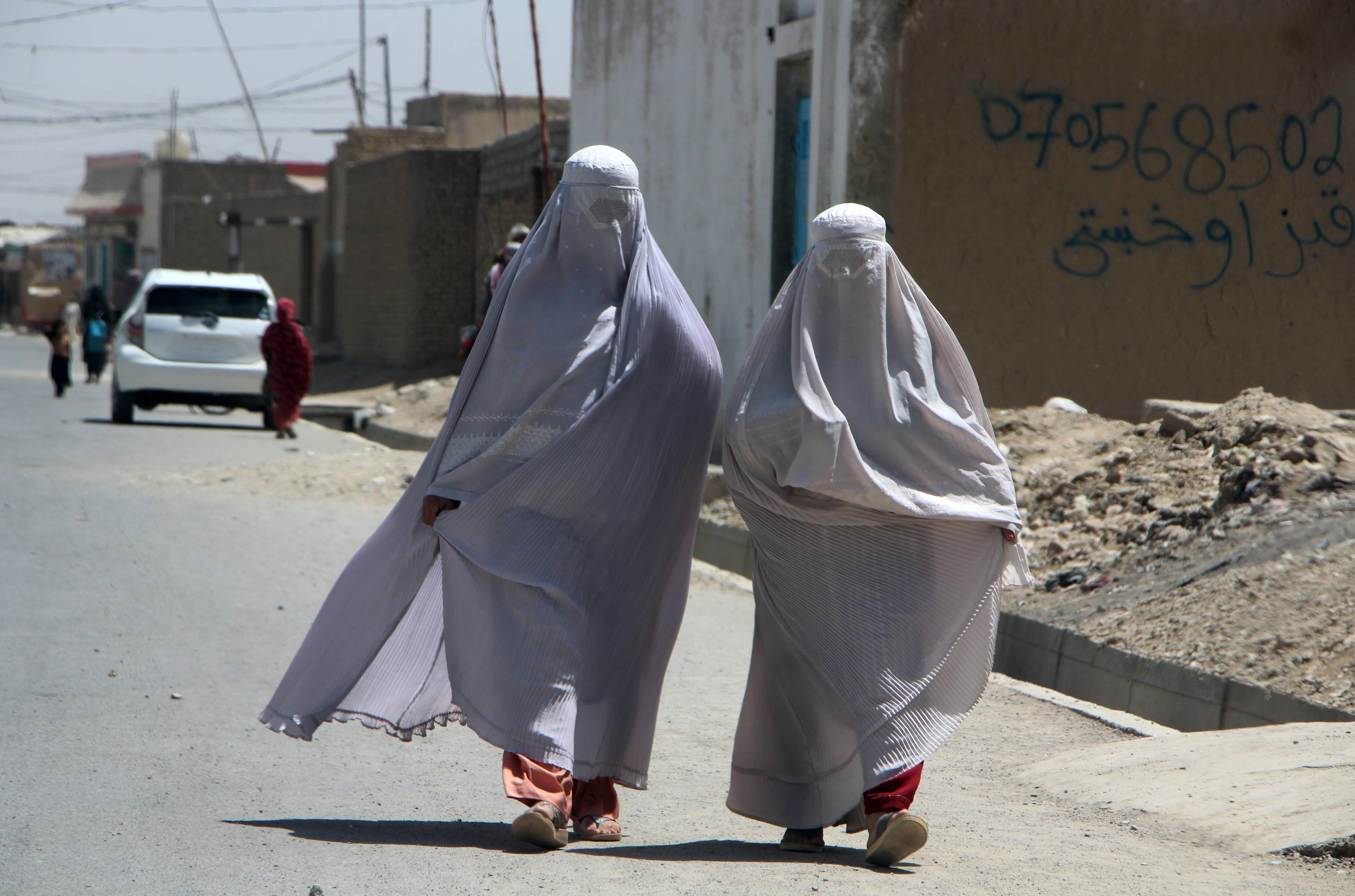 dos mujeres visitiendo burkas caminan por las calles de afganistán