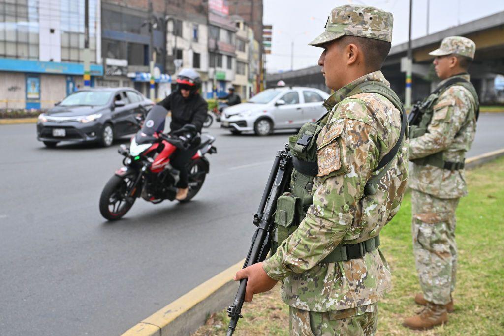 Dos militares con armas largas vigilan en el arcén de una vía en Perú. 