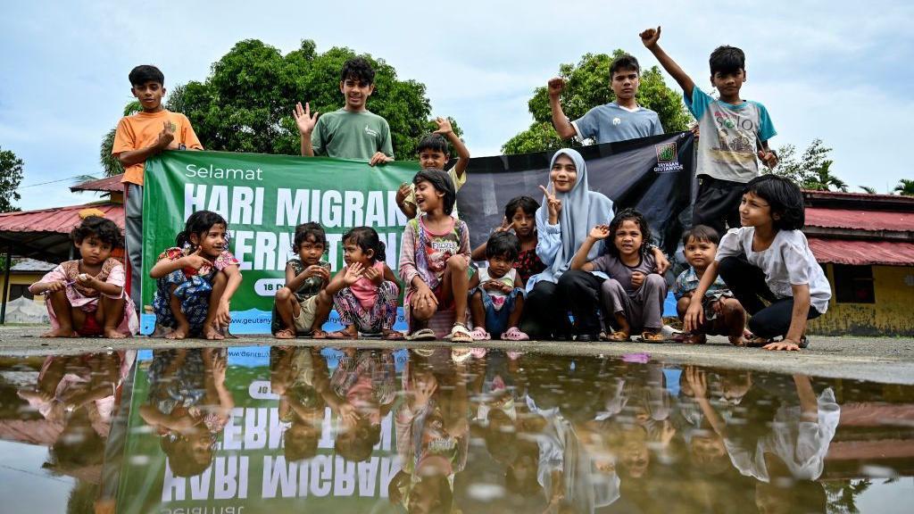 Anak-anak dan relawan berpose dengan spanduk Hari Migran Internasional di kamp pengungsi Rohingya di Padang Tiji, provinsi Aceh, Indonesia pada 18 Desember 2024.