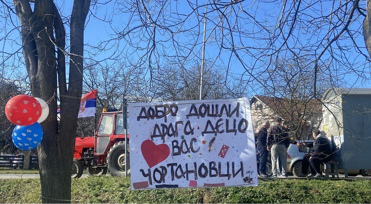 baloni, zastava Srbije i ljudi sa plakatom sede i čekaju studente