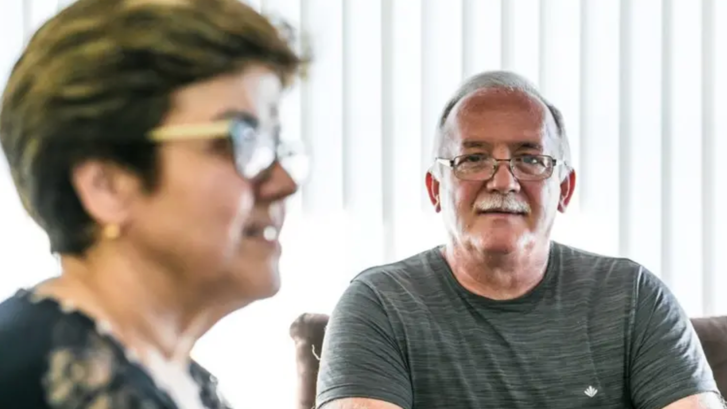 Mulher de óculos perfilada e, à sua direita, homem de bigode, cabelos brancos, pele clara