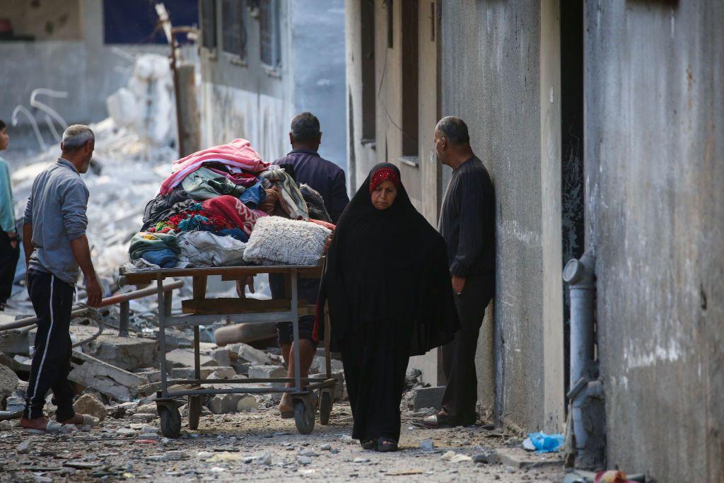 Unos hombres transportan objetos que recuperaron de entre los escombros de sus casas, mientras una mujer camina frente a ellos, tras un ataque israelí en el campo de refugiados de Nuseirat, en la zona central de la Franja de Gaza, el 18 de marzo de 2025.  (Foto: Eyad BABA / AFP vía Getty Images)