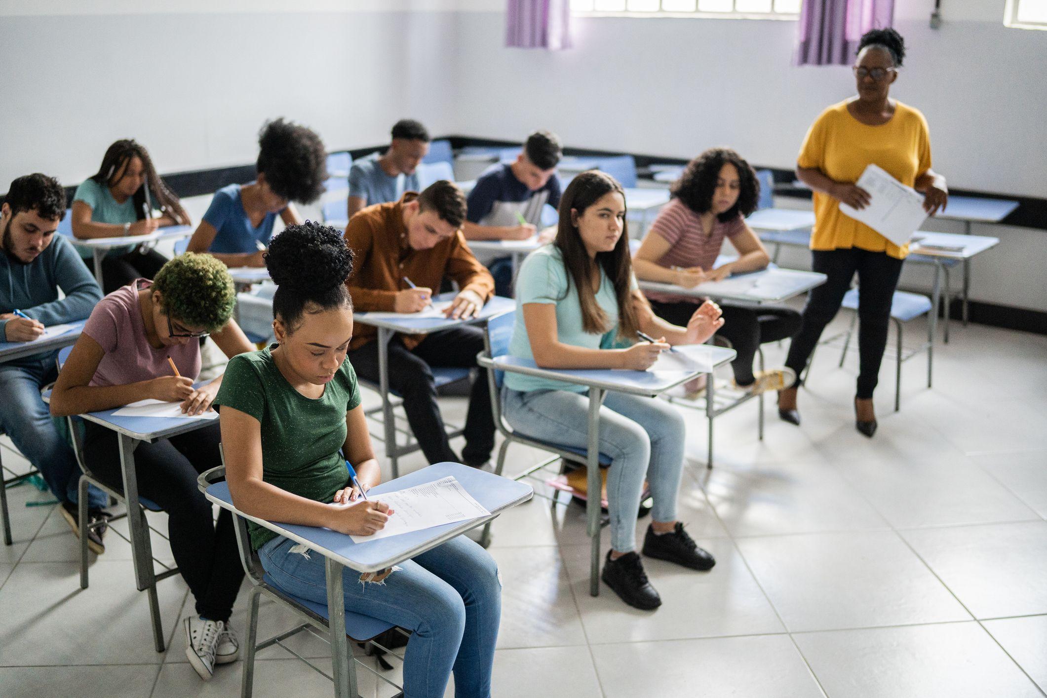 Sala de aula com alunos diversos preenchendo prova