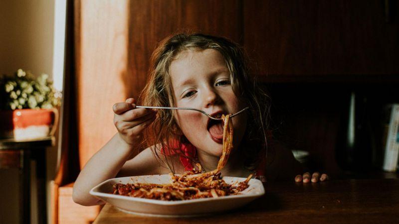 Criança comendo macarrão com molho vermelho