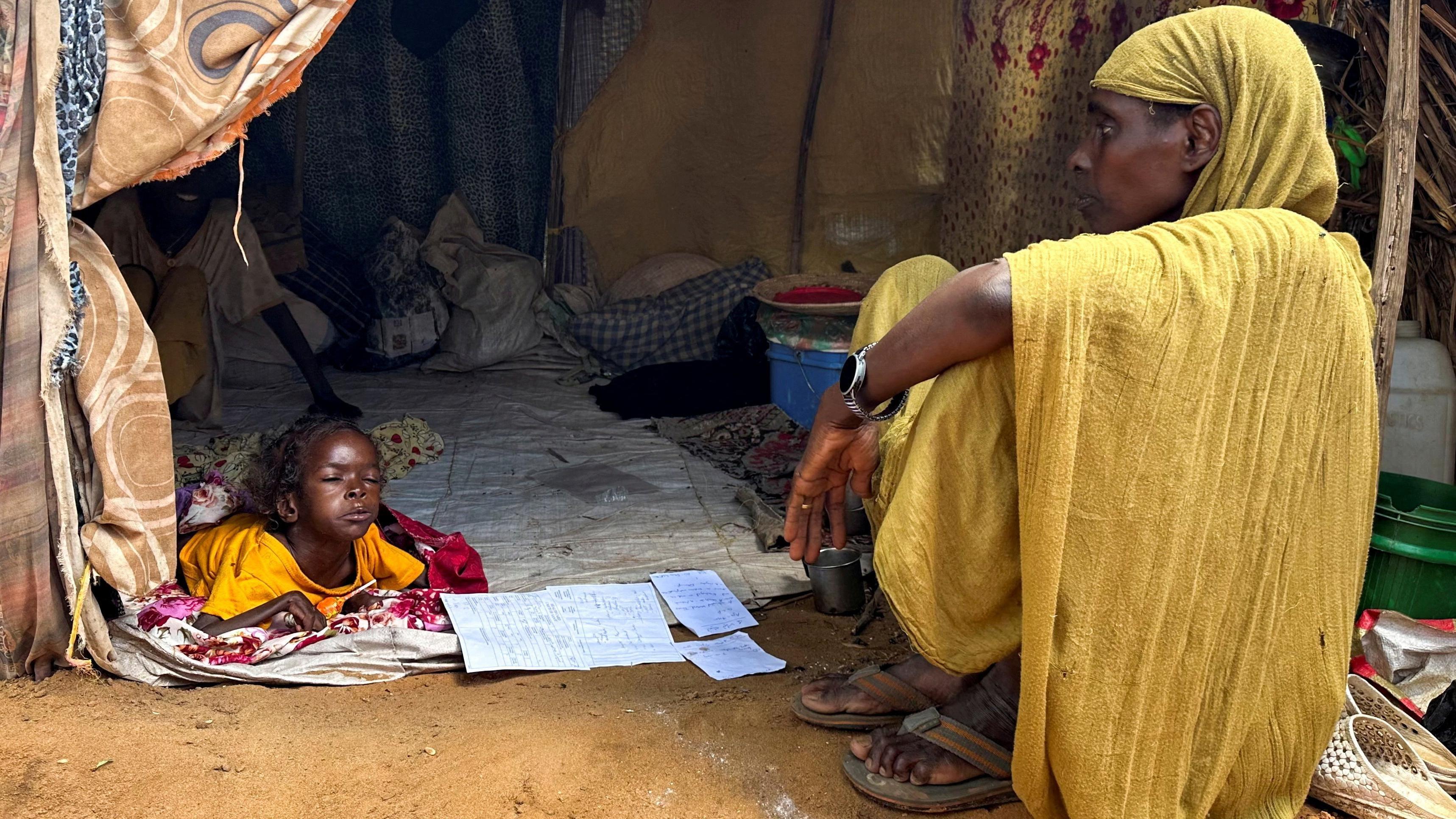 صورة تظهر امرأة سودانية نازحة تجلس إلى جانب طفلة عند مدخل خيمة في مخيم زمزم للنازحين في شمال دارفور.