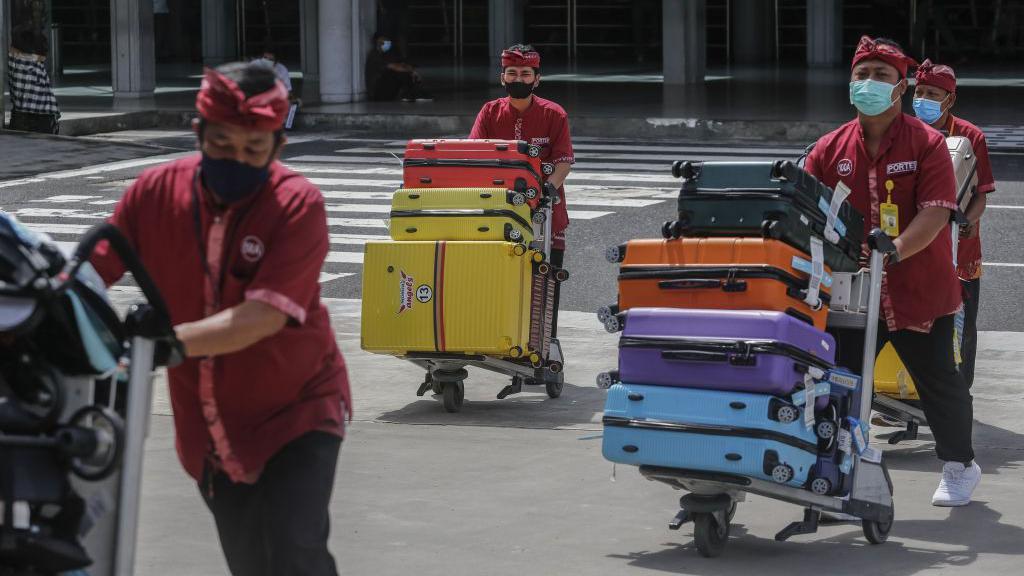 Petugas bandara membawa barang bawaan pelancong yang datang menjelang musim libur Natal dan Tahun Baru di tengah pandemi Covid-19 di Bandara I Gusti Ngurah Rai, Bali.