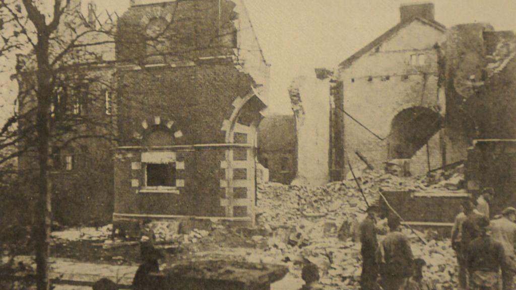 Pessoas na rua observam sinagoga destruída