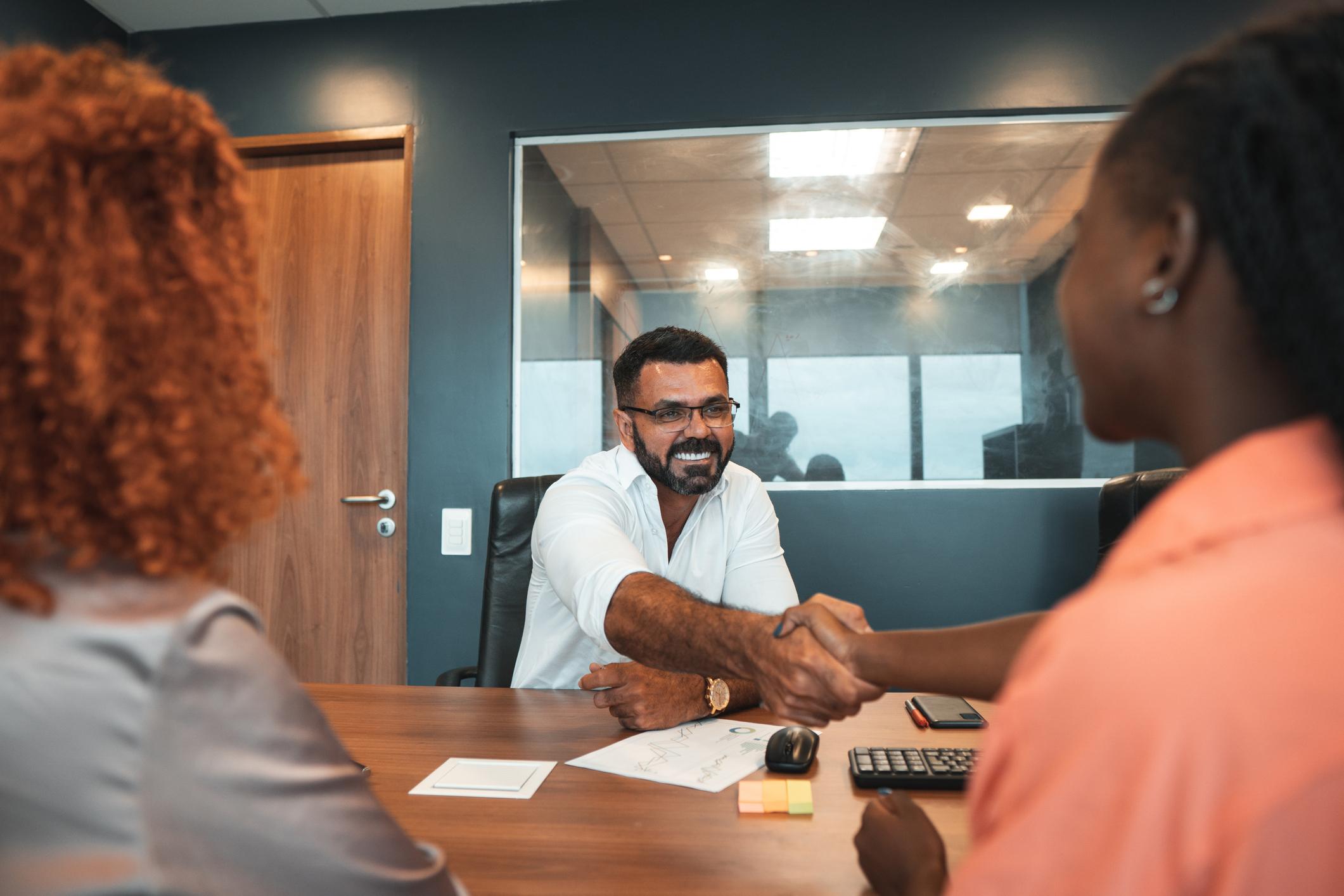 Homem e mulher dando um aperto de mão em ambiente corporativo