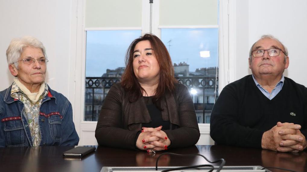 Francesca Satta no meio de uma senhora e de um senhor, os três sentados à mesa. 