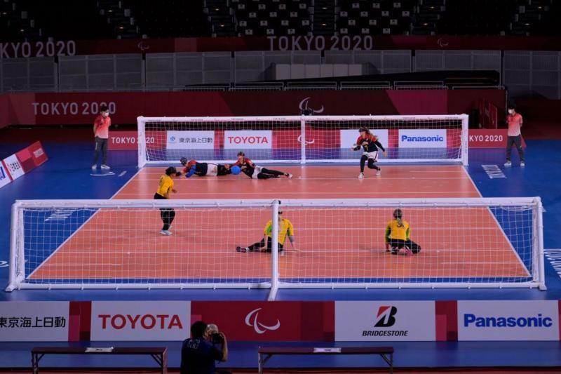 Plano amplo mostra uma partida de goalball do ângulo traseiro da quadra