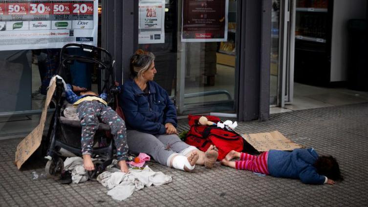 Una mujer con dos niños pidiendo limosna afuera de un supermercado en Buenos Aires.