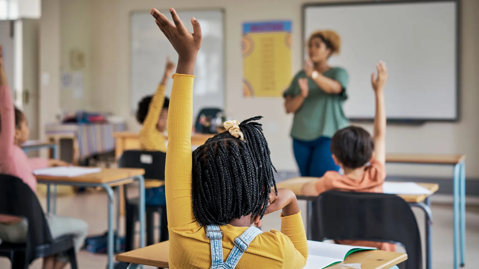Menina negra levantando a mão esquerda em sala de aula
