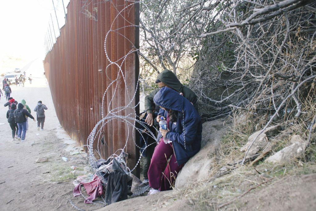 Migrantes pasando por un hueco en el muro fronterizo entre Baja California, México, y California, Estados Unidos.