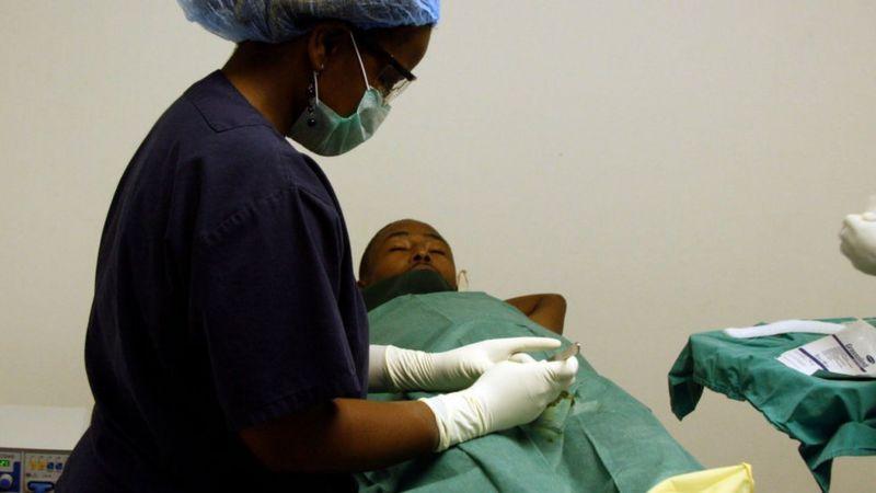 Médica com bisturi na mão prestes a realizar circuncisão em paciente
