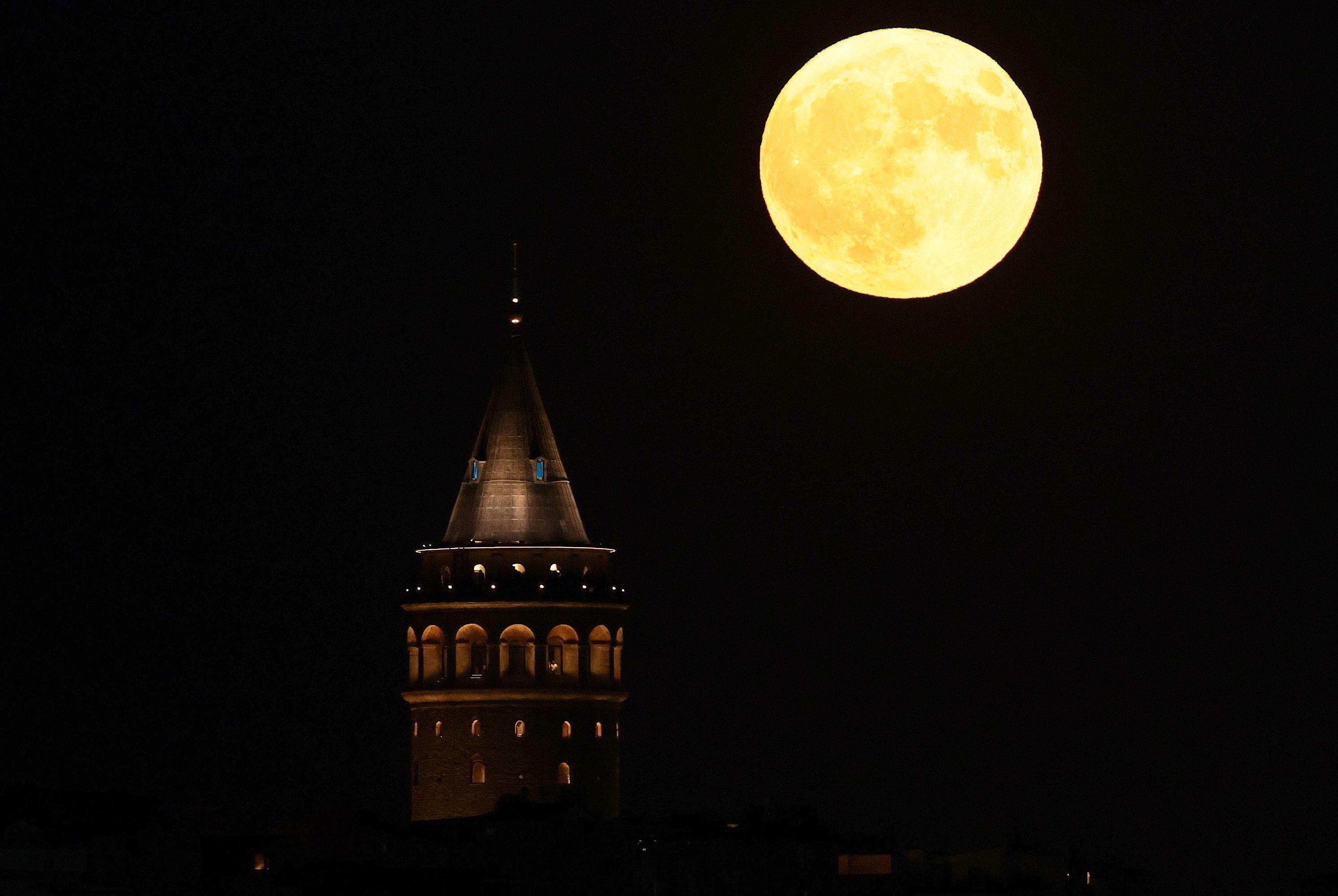 Lua amarelada ao lado de uma torre histórica iluminada 