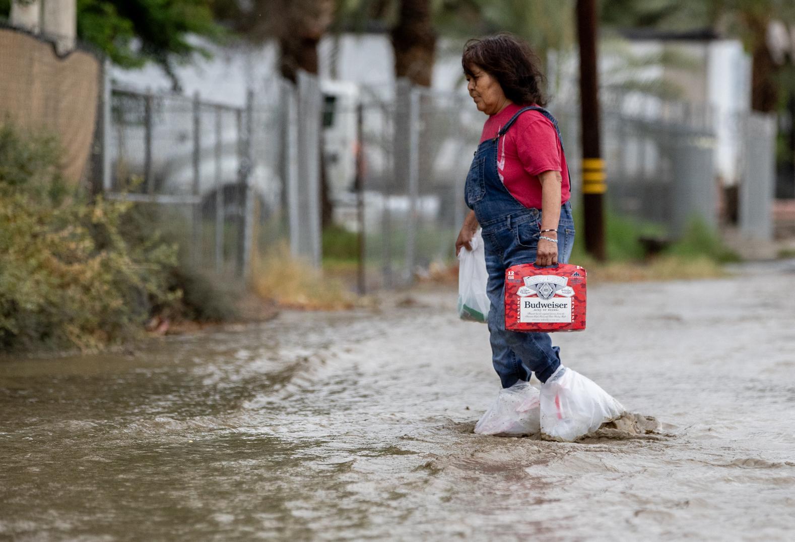 Nannie Auclair usa bolsas de plástico en sus pies para atravesar la inundación mientras carga una caja de cerveza que acaba de comprar en un mercado del vecindario en Thermal, California.