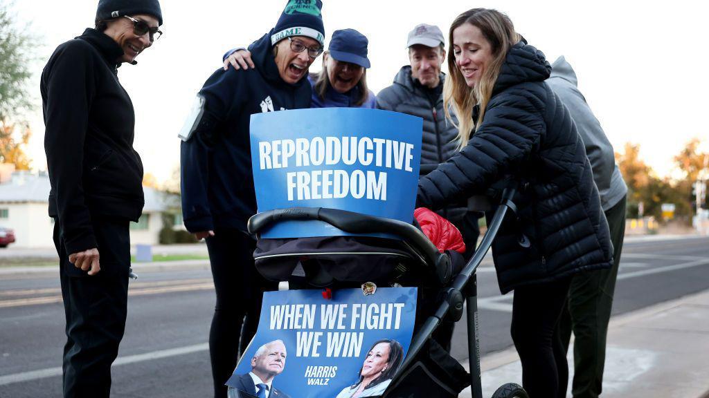 Julie Bufkin (derecha) conversa con los vecinos mientras empuja el cochecito de su hija Alice, adornado con carteles que dicen "Libertad reproductiva" y "Cuando luchamos, ganamos", el 5 de noviembre de 2024 en Tempe, Arizona. La aprobación de la Proposición 139 en Arizona codificaría “el derecho fundamental al aborto” en Arizona. (Foto de Mario Tama/Getty Images)
