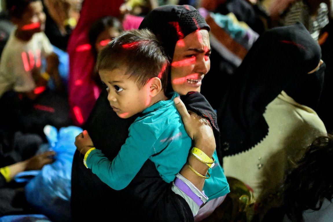 A Rohingya Muslim woman reacts while holding her child, as they are relocated from their temporary shelter in Banda Aceh, Indonesia following protests on 27 December 2023