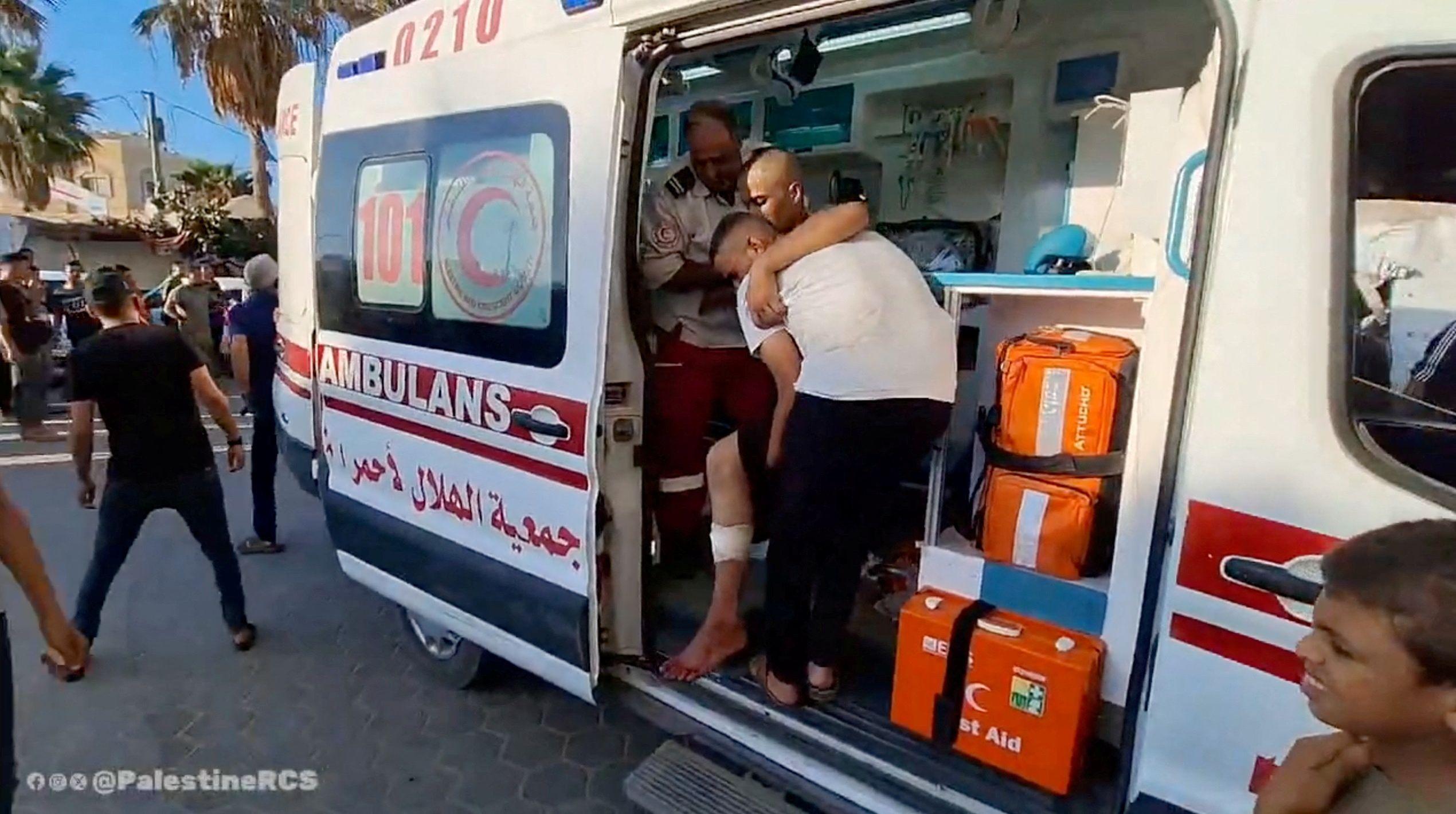 أشخاص يساعدون رجلاً بينما يقوم أعضاء جمعية الهلال الأحمر الفلسطيني بنقل الجرحى الفلسطينيين إلى مستشفى شهداء الأقصى من مخيم النصيرات في دير البلح.