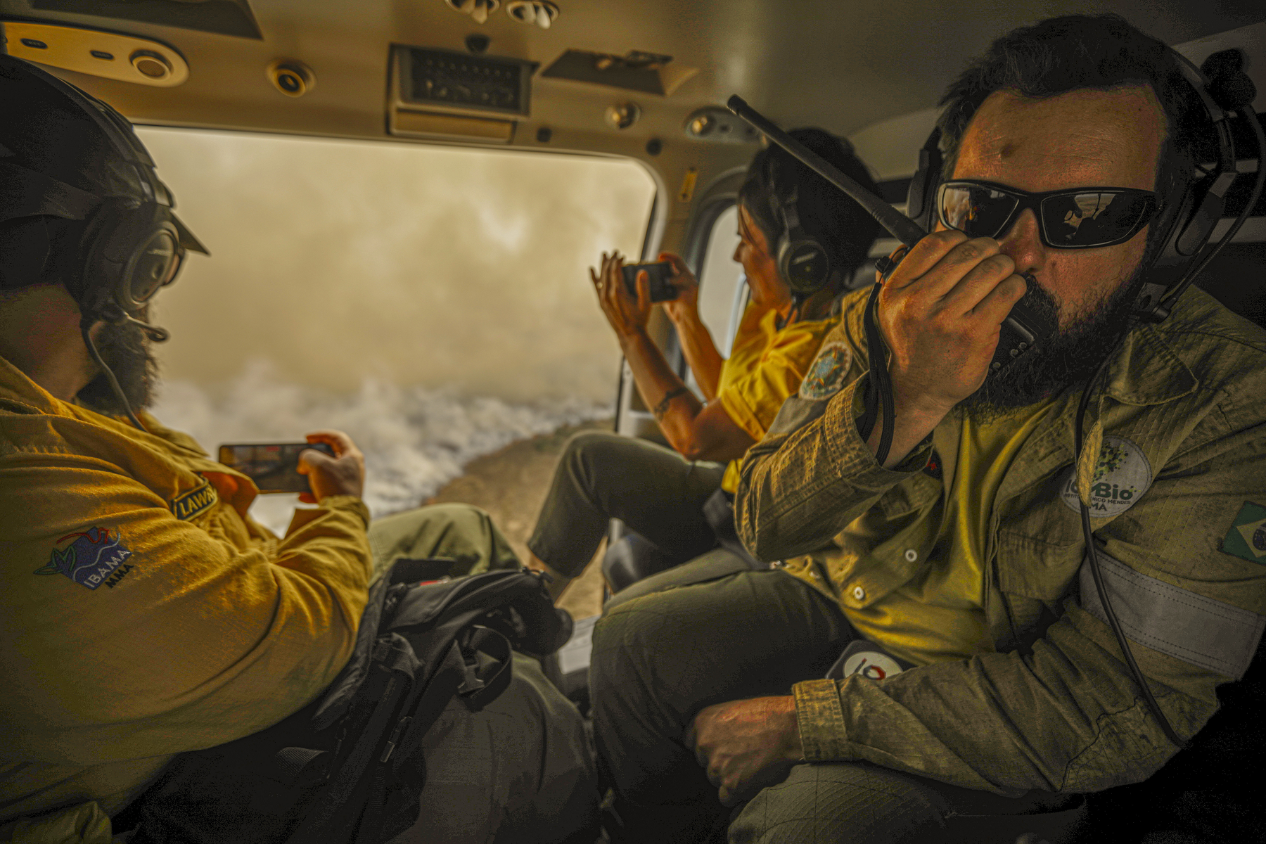 Coordenador do combate ao incêndio florestal que atinge o Pantanal, Heoder Marques (d), acompanhado de fiscais do Ibama, aciona por rádio as equipes em terra sobre o movimento do fogo, durante sobrevoo em um helicóptero da Polícia Federal Rodoviaria (PRF)