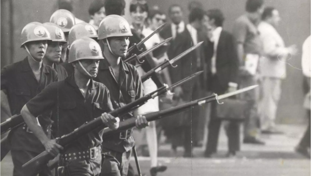 Foto em preto e branco de policiais armados em uma rua 