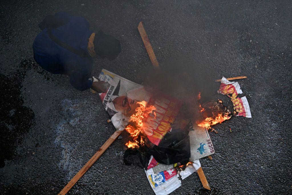Un opositor al gobierno del presidente venezolano Nicolás Maduro quema carteles de la campaña de Maduro durante una protesta en el barrio de Petare en Caracas 