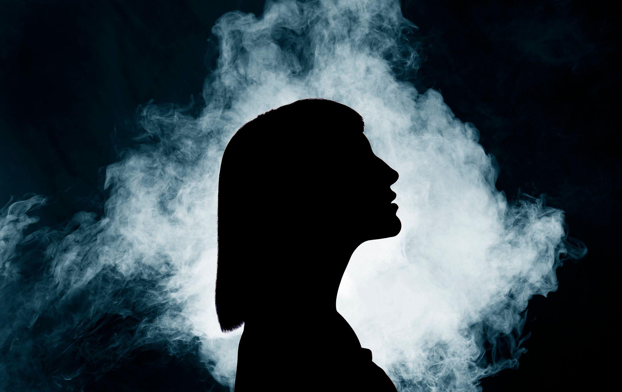 Una silueta de la cabeza de una mujer en medio de una nube de humo iluminada por una luz