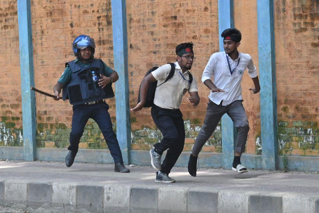 Seorang polisi mengejar dua mahasiswa demonstran di Dhaka.