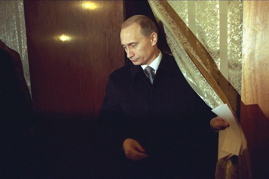 Putin vota nas eleições parlamentares da Rússia em 1999. Ele segura veste um terno preto e gravata e segura um papel nas mãos, ao mesmo tempo em que abre uma cortina.