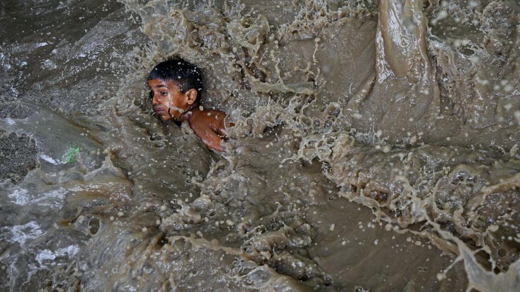 Seorang anak laki-laki terjebak genangan banjir tepi Sungai Yamuna yang meluap akibat akibat musim hujan