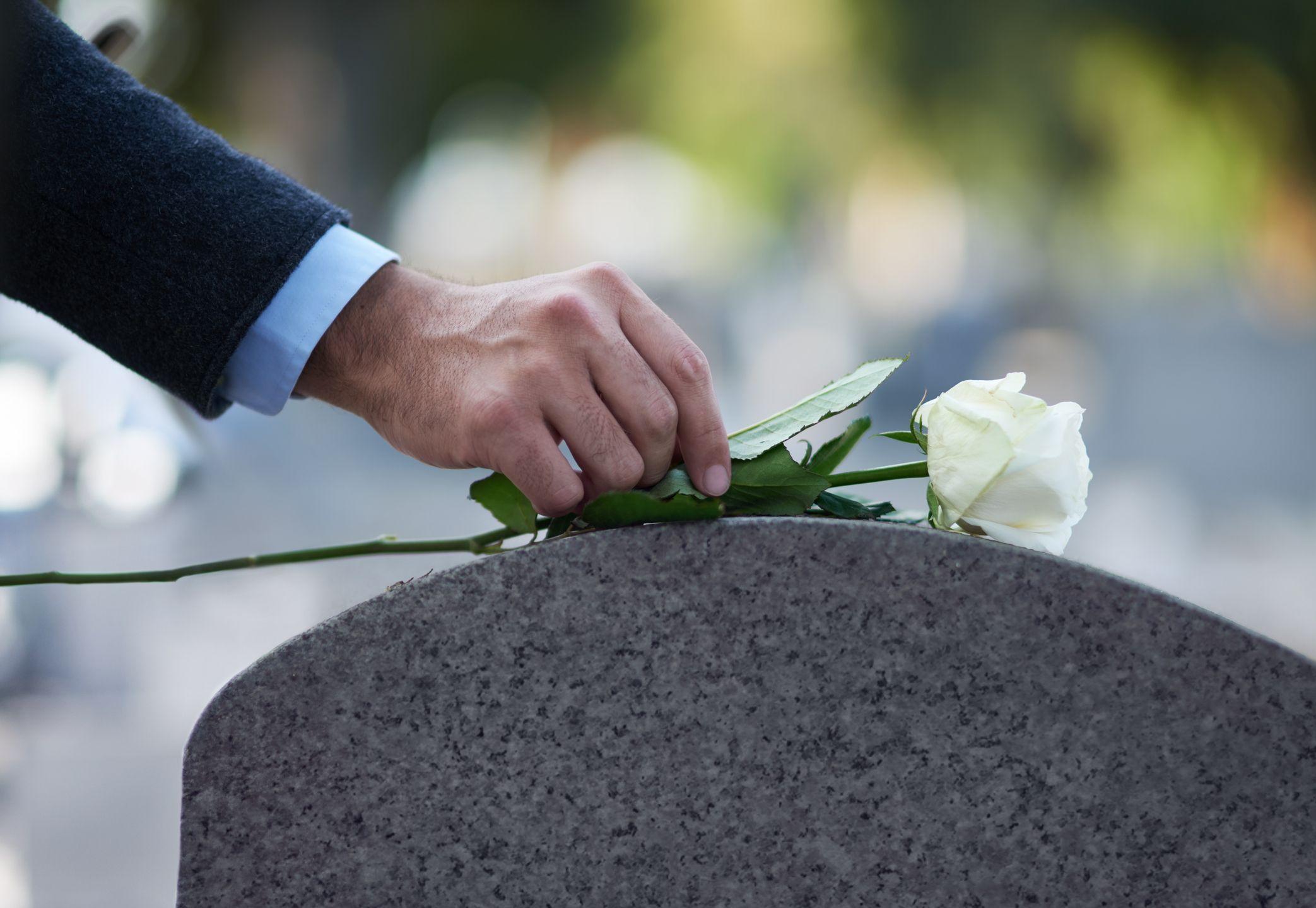 Un hombre pone una rosa blanca sobre una lápida