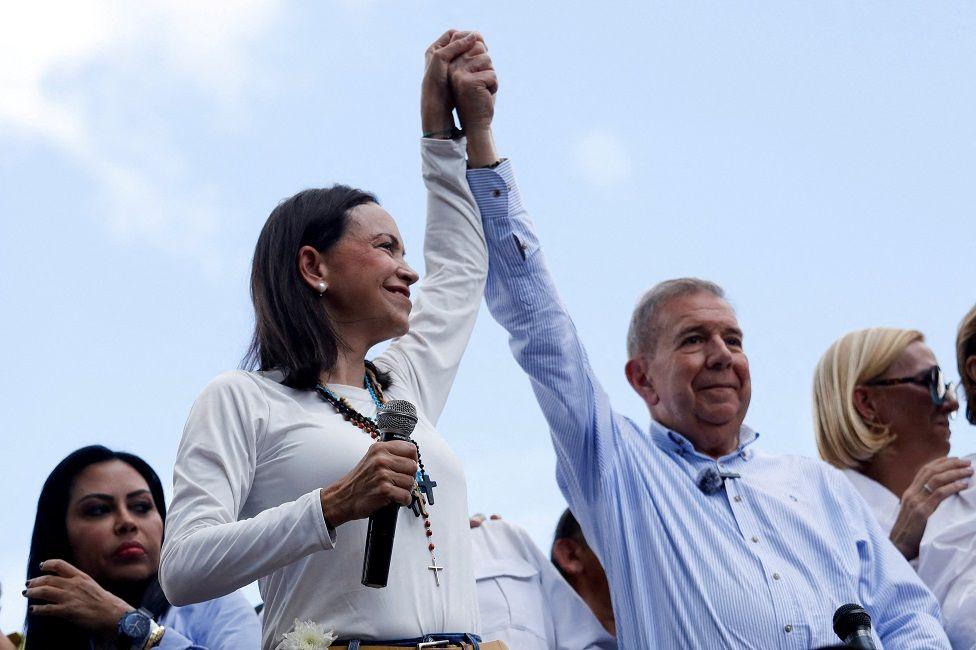 María Corina Machado e Edmundo González levantando os braços em sinal de apoio mútuo durante um evento público