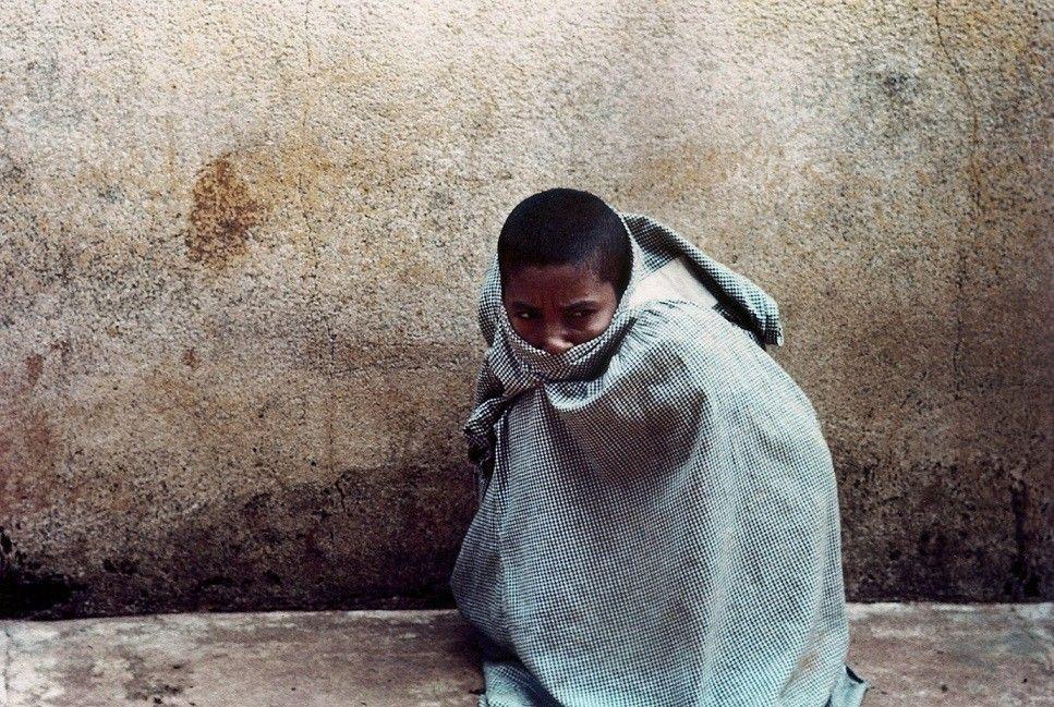 Paciente agachado e encolhido perto de muro, envolto em uma roupa